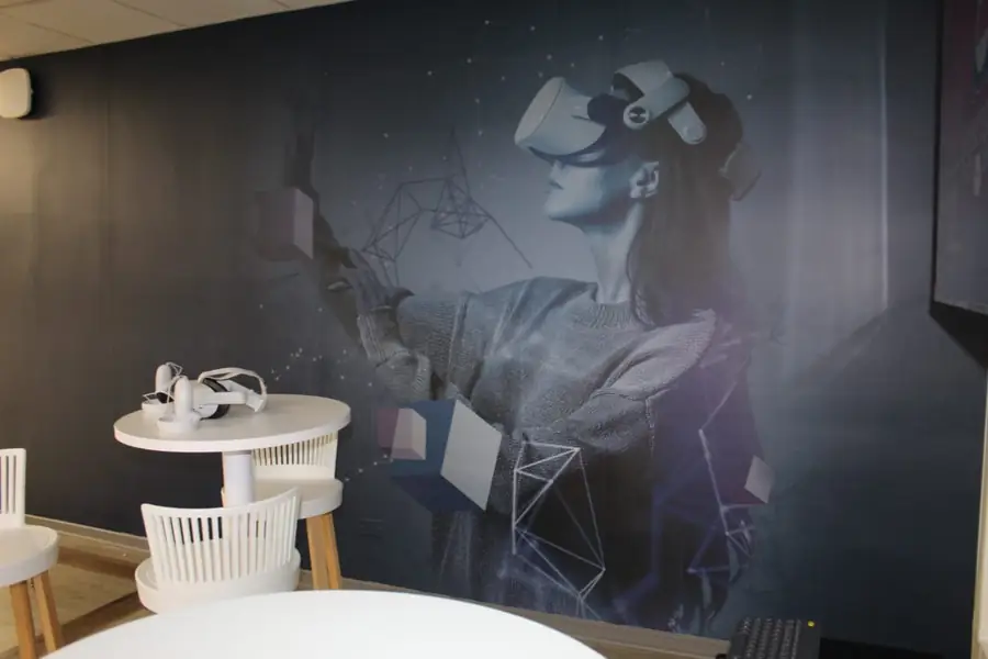 Mesa y sillas frente al mural de la Sala de Realidad Virtual de la Biblioteca Campus República UNAB.